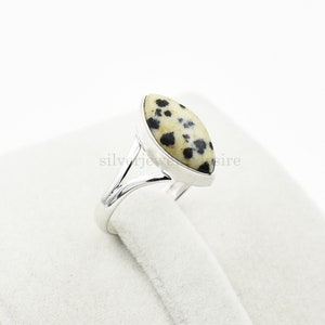May include: A silver ring with a dalmatian jasper stone. The stone is a light brown color with black spots.