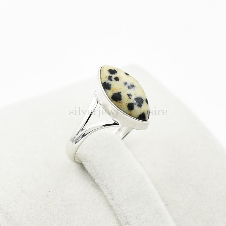 May include: A silver ring with a dalmatian jasper stone. The stone is a light brown color with black spots.