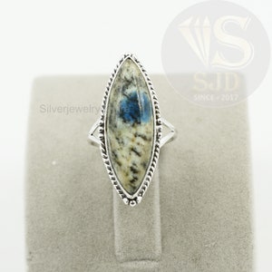 May include: A silver ring with a blue and white marbled stone set in a marquise shape. The ring has a braided design around the stone.