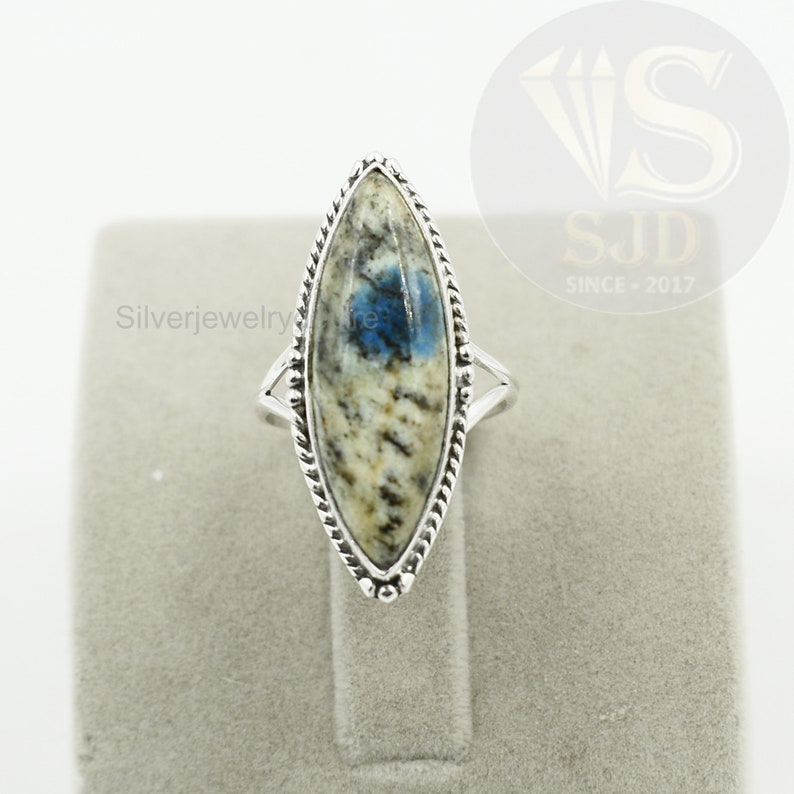May include: A silver ring with a blue and white marbled stone set in a marquise shape. The ring has a braided design around the stone.