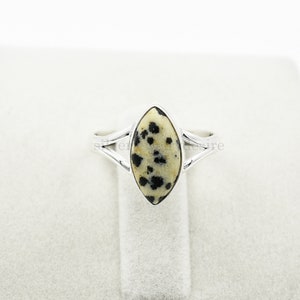 May include: A silver ring with a marbled oval-shaped stone. The stone is white with black spots.