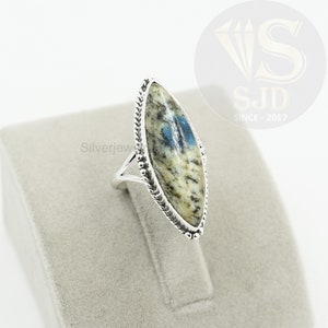 May include: A silver ring with a blue and white oval-shaped stone set in a silver bezel. The stone has a marbled pattern and is surrounded by a silver braided band.