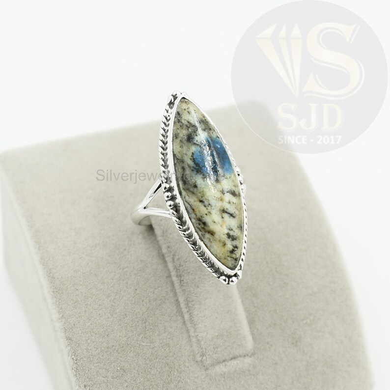 May include: A silver ring with a blue and white oval-shaped stone set in a silver bezel. The stone has a marbled pattern and is surrounded by a silver braided band.