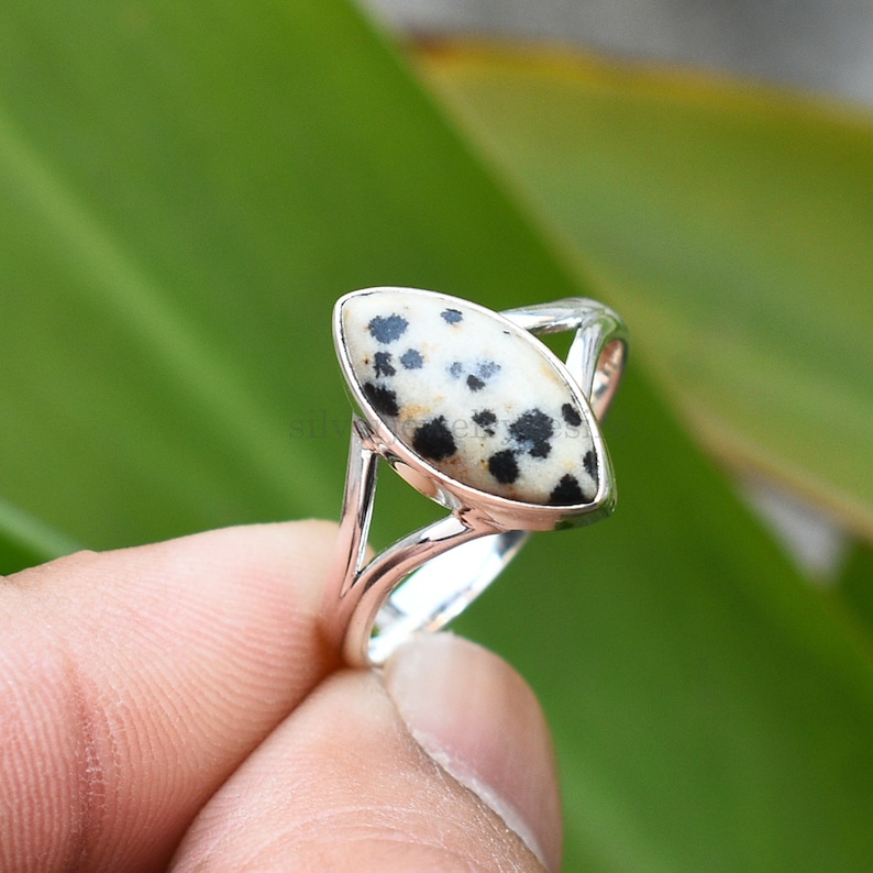 May include: A silver ring with a dalmatian jasper stone. The stone is a marbled pattern of black and white.