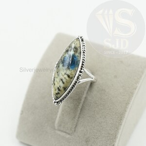 May include: A silver ring with a blue and white oval-shaped gemstone set in a silver bezel. The ring has a rope-like design around the edge of the bezel.