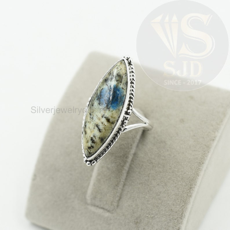 May include: A silver ring with a blue and white oval-shaped gemstone set in a silver bezel. The ring has a rope-like design around the edge of the bezel.