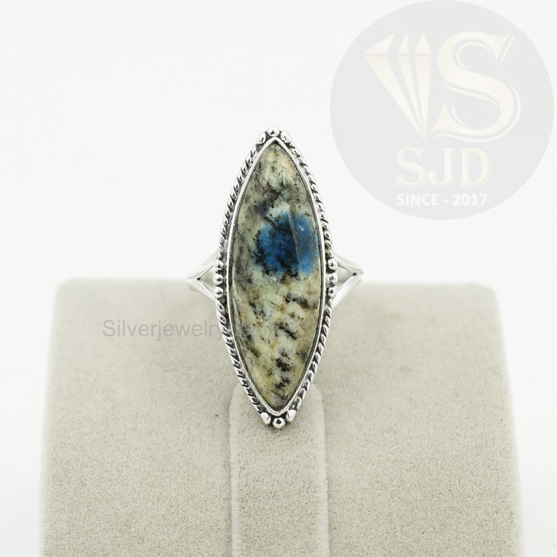 May include: A silver ring with a blue and white marbled stone set in a marquise shape. The ring is set in a silver band with a rope-like design.