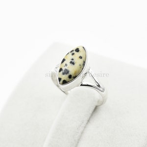 May include: A silver ring with a dalmatian jasper stone. The stone is a light brown color with black spots.
