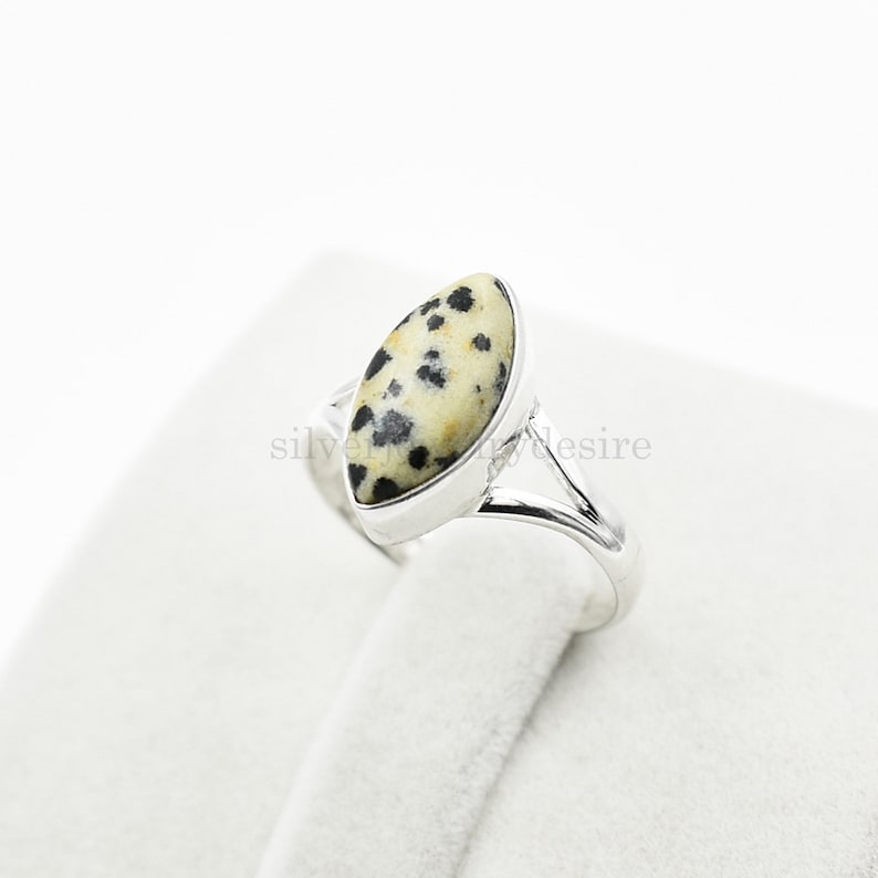 May include: A silver ring with a dalmatian jasper stone. The stone is a light brown color with black spots.