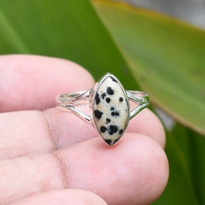 May include: A silver ring with a black and white dalmatian jasper stone. The ring has a delicate, open design.