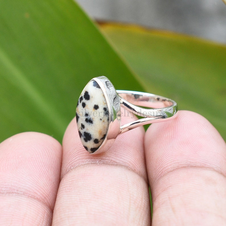 May include: A silver ring with a black and white dalmatian jasper oval gemstone. The ring has a simple, elegant design.