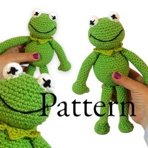 Puede incluir: Peluche de rana verde tejido a ganchillo con detalles en blanco y negro. La rana tiene un cuello amarillo y está sostenida por manos. La palabra "Pattern" está escrita en negro en la imagen. El artículo es hecho a mano.