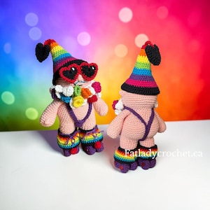 May include: Two crocheted figures wearing rainbow-striped hats with black heart-shaped pom-poms, heart-shaped sunglasses, and rainbow-colored roller skates. One figure wears a colorful crocheted neck ruff. The text Fatladycrochet.ca is visible.