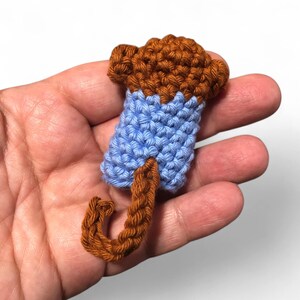 May include: A small crocheted monkey toy with a brown body, blue shirt, and a curled tail.