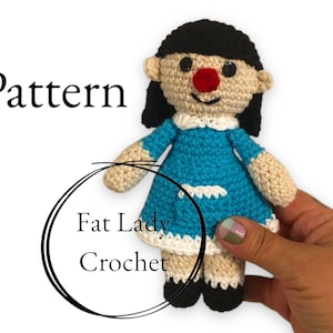 Puede incluir: Muñeca de ganchillo con cabello negro, nariz roja y vestido azul. La muñeca tiene cuello y ribete blancos. El texto "Pattern" y "Fat Lady Crochet" son visibles en la imagen.