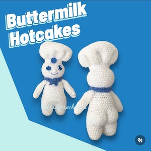 May include: Two white crochet figures resembling the Pillsbury Doughboy, one facing forward and the other backward. Both figures wear a chef's hat and a blue collar. The text "Buttermilk Hotcakes" is at the top of the image.