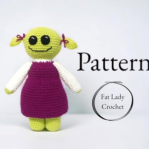 Puede incluir: Muñeca verde de crochet con un vestido rosa, mangas blancas y ojos negros. La muñeca tiene una expresión feliz y coletas. El texto "Pattern" y "Fat Lady Crochet" es visible en la imagen.