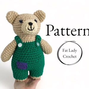 May include: A beige crocheted teddy bear wearing green overalls with white buttons and a small purple patch on the leg. The text Pattern and Fat Lady Crochet are printed to the right of the bear in black serif and sans-serif fonts.