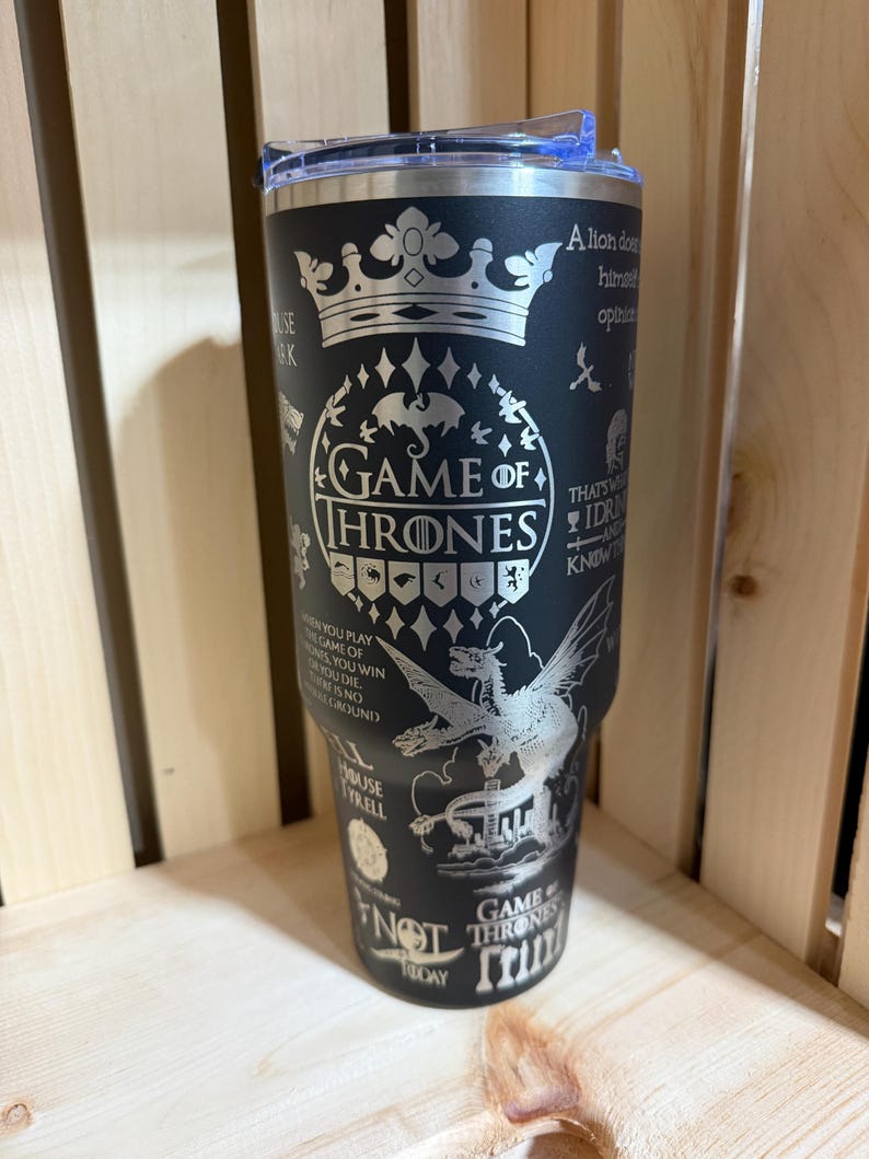 Pu&ograve; includere: Bicchiere in acciaio inossidabile nero con un design argentato. Presenta le parole "Game of Thrones", citazioni e simboli. Il design include una corona, un drago e altre immagini della serie. Il bicchiere ha un coperchio trasparente.