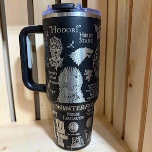 Pu&ograve; includere: Bicchiere termico nero con manico e coperchio neri. Il bicchiere presenta disegni incisi e testo della serie Game of Thrones, tra cui "Hodor!", Casa Stark e il Trono di Spade. Il bicchiere &egrave; progettato per mantenere le bevande fredde o calde.