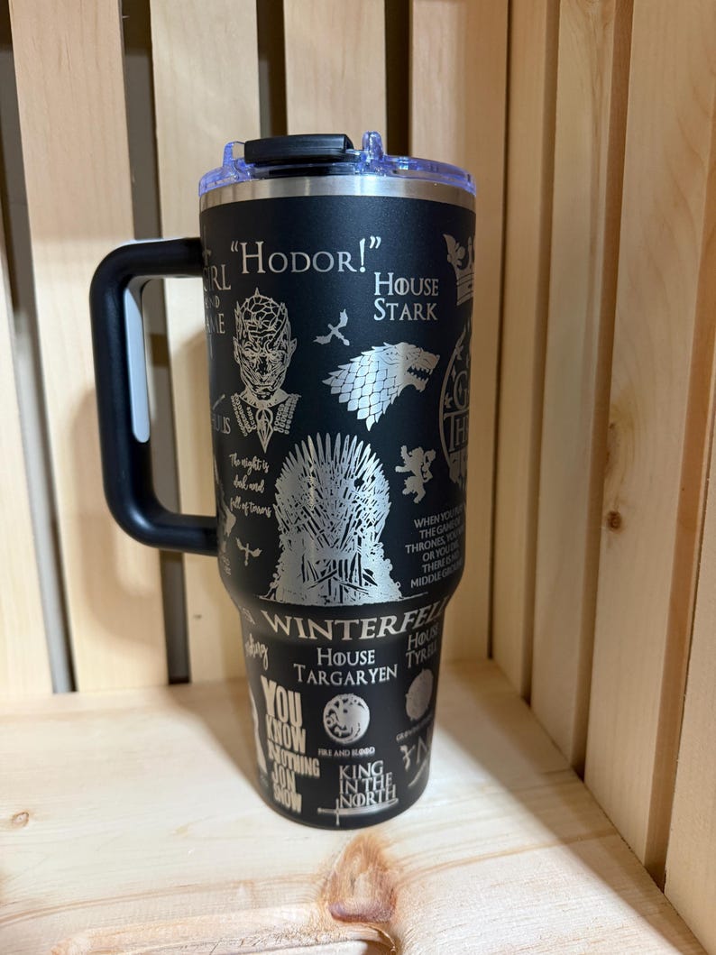 Pu&ograve; includere: Bicchiere termico nero con manico e coperchio neri. Il bicchiere presenta disegni incisi e testo della serie Game of Thrones, tra cui "Hodor!", Casa Stark e il Trono di Spade. Il bicchiere &egrave; progettato per mantenere le bevande fredde o calde.