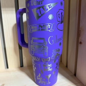 Pu&ograve; includere: Un bicchiere viola con manico e coperchio argentato. Il bicchiere &egrave; decorato con grafica e testo argentati, tra cui "Diner", "YALE", "Miss Patty's School of Ballet" e "Gilmore". Il bicchiere &egrave; alto circa 25 cm.
