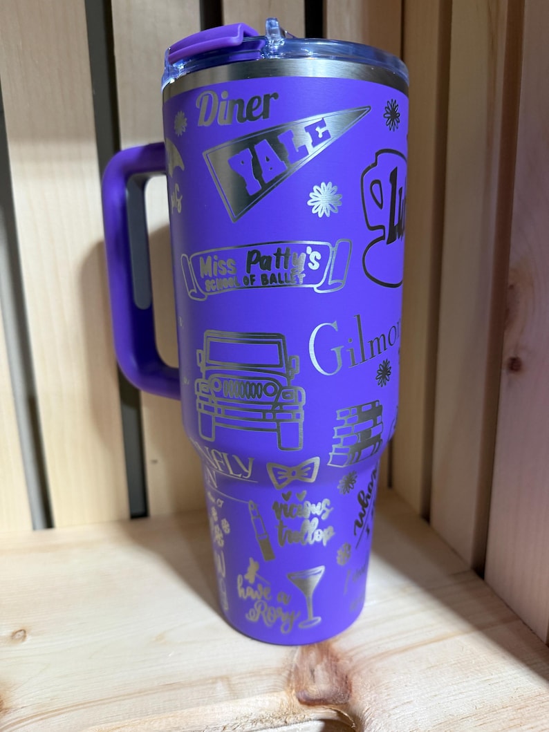 Pu&ograve; includere: Un bicchiere viola con manico e coperchio argentato. Il bicchiere &egrave; decorato con grafica e testo argentati, tra cui "Diner", "YALE", "Miss Patty's School of Ballet" e "Gilmore". Il bicchiere &egrave; alto circa 25 cm.