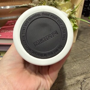 May include: White and black insulated water bottle base with text that reads "Do not use in freezer, microwave, oven and stovetop. Hand wash only, BPA free." The base has a black center with care symbols.