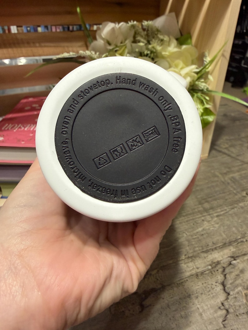May include: White and black insulated water bottle base with text that reads "Do not use in freezer, microwave, oven and stovetop. Hand wash only, BPA free." The base has a black center with care symbols.