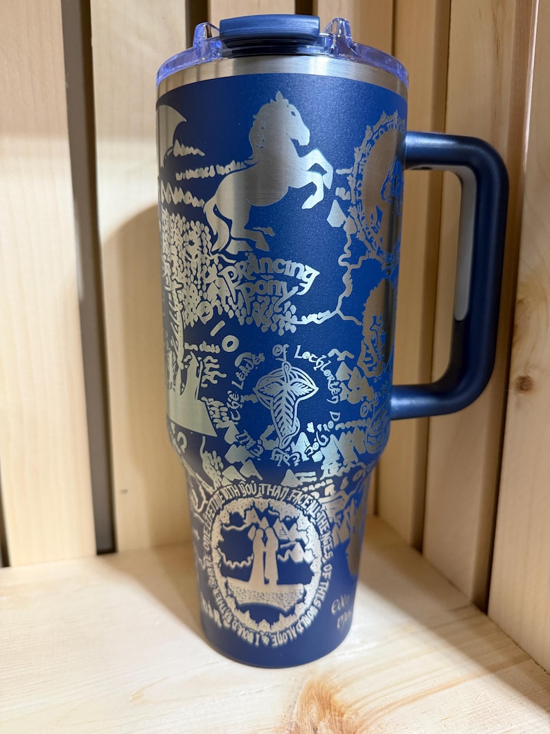 May include: A blue insulated travel mug with a silver design featuring a horse, map, and text. The mug has a handle and a lid. The text includes "Dancing Pony" and other phrases. The mug is designed for hot or cold beverages.