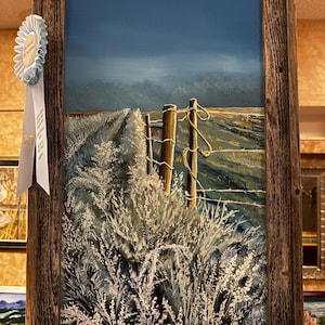 May include: An oil painting of a rural landscape with a wooden fence and tall, wispy plants in the foreground. The artwork is framed in a rustic, weathered wood frame. A light blue ribbon is attached to the frame.