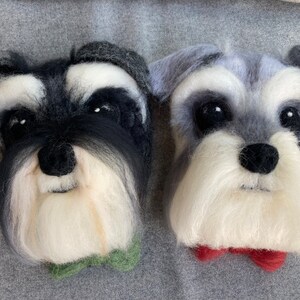 Puede incluir: Dos retratos en miniatura de perros schnauzer de fieltro, con pelo blanco y negro, uno con una pajarita verde y el otro con una pajarita roja.