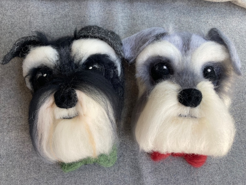 Puede incluir: Dos retratos en miniatura de perros schnauzer de fieltro, con pelo blanco y negro, uno con una pajarita verde y el otro con una pajarita roja.