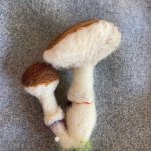 Puede incluir: Dos setas de fieltro, una marr&oacute;n y otra blanca, con una base verde. Las setas est&aacute;n apiladas una encima de la otra.