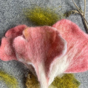 Puede incluir: Un hongo de fieltro rosa y blanco con una superficie texturizada. El hongo est&aacute; hecho de lana y tiene una forma delicada y org&aacute;nica.