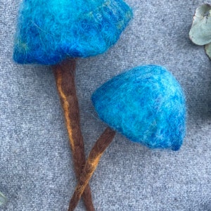 Puede incluir: Dos setas de fieltro azul con tallos marrones. Las setas est&aacute;n hechas de fieltro de lana y tienen una textura peluda.