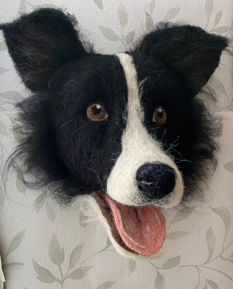 Puede incluir: Una escultura de fieltro de la cabeza de un perro Border Collie, en blanco y negro, con la lengua rosa que sobresale. El perro tiene ojos marrones y la nariz negra.