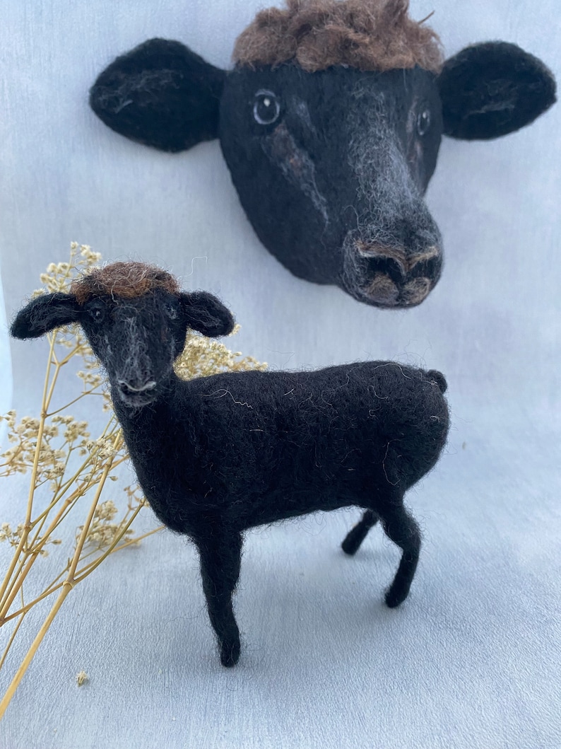 Puede incluir: Dos ovejas de fieltro de lana negra, una oveja de cuerpo entero de pie sobre una superficie blanca, la otra una cabeza de oveja montada en la pared.