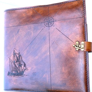 May include: A brown leather journal with a compass and a ship engraved on the front cover. The journal has a brass clasp.