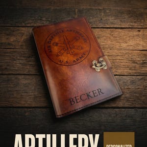 May include: A brown leather journal with the text "Air Defense Artillery U.S. Army" and "Becker" engraved on the cover. The journal has a metal clasp and the words "Handmade & Rustic" and "Leader Book" are also visible.