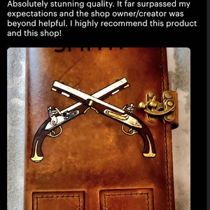 May include: A brown leather journal with a brass clasp and a gold-colored illustration of two crossed pistols. The journal has two pockets on the front.