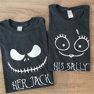 K&ouml;nnte beinhalten: Zwei dunkelgraue T-Shirts mit wei&szlig;en Grafikdesigns. Ein Shirt zeigt ein wei&szlig;es Jack Skellington Gesicht mit dem Text "Her Jack" und das andere Shirt zeigt ein wei&szlig;es Sally Gesicht mit dem Text "His Sally".