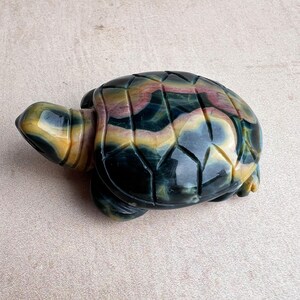 May include: A carved stone turtle figurine. The turtle has a detailed shell with a pattern of green, yellow, and red hues. The head and legs are also carved with similar colours. The figurine is a decorative item.