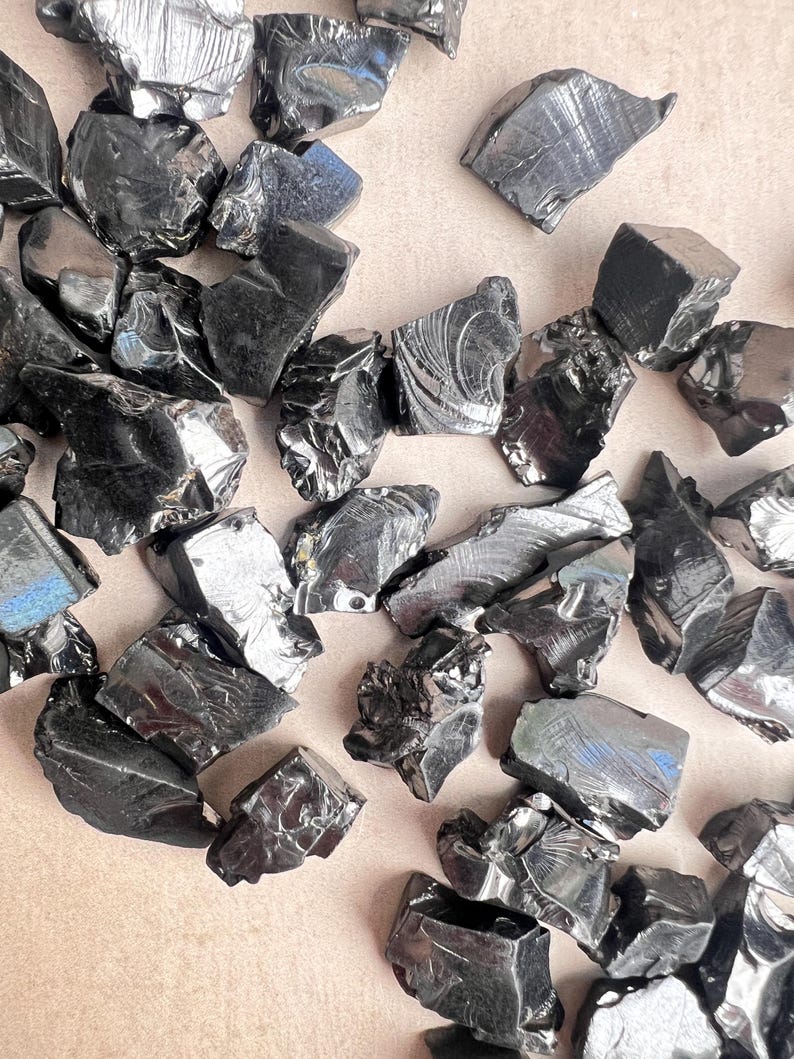 May include: A collection of raw, polished obsidian stones. The stones are a deep, reflective black with irregular shapes and a glossy surface. The arrangement suggests a natural, earthy aesthetic, suitable for crystal enthusiasts or those interested in geology.