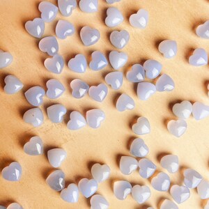 Puede incluir: Una colecci&oacute;n de peque&ntilde;as cuentas en forma de coraz&oacute;n de color azul claro dispersas sobre una superficie marr&oacute;n claro. Las cuentas tienen un aspecto liso y pulido y est&aacute;n distribuidas uniformemente, creando un patr&oacute;n de corazones.