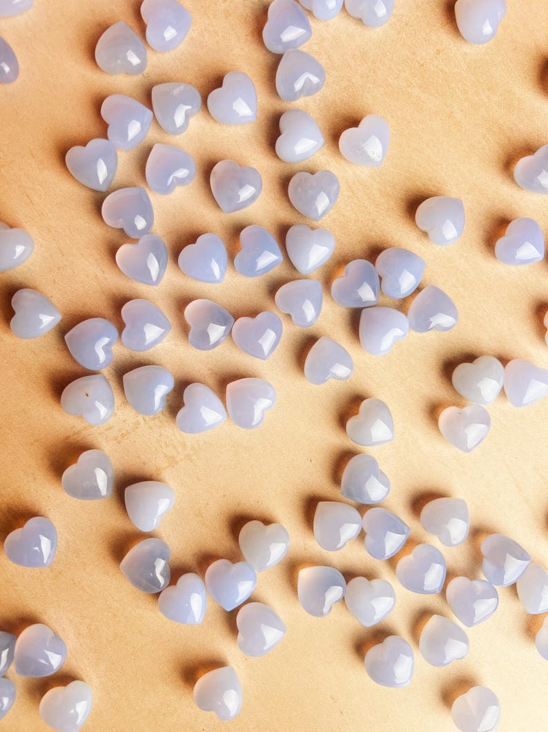 Puede incluir: Una colecci&oacute;n de peque&ntilde;as cuentas en forma de coraz&oacute;n de color azul claro dispersas sobre una superficie marr&oacute;n claro. Las cuentas tienen un aspecto liso y pulido y est&aacute;n distribuidas uniformemente, creando un patr&oacute;n de corazones.