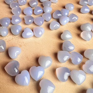 Puede incluir: Una colecci&oacute;n de peque&ntilde;as piedras en forma de coraz&oacute;n en tonos azul p&aacute;lido y lavanda. Las piedras pulidas est&aacute;n dispersas sobre una superficie marr&oacute;n claro, creando una est&eacute;tica suave y rom&aacute;ntica. Estas piedras en forma de coraz&oacute;n son ideales para la fabricaci&oacute;n de joyas o manualidades.