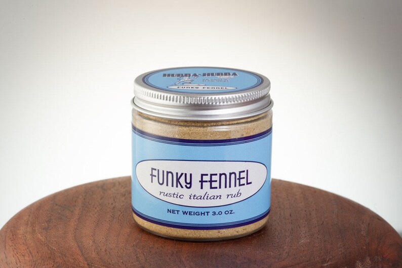 May include: A glass jar with a silver lid containing a brown spice blend. The label is blue and white and reads "Funky Fennel rustic italian rub" and "NET WEIGHT 3.0 OZ."
