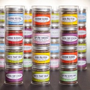 May include: A set of six clear glass jars filled with different spice blends. Each jar has a colorful label with a unique name and description. The names include "Funky Fennel", "Hubba Rubba", "Rub My Fish", "Hubba Bubbacue", "Dip Me Daddo", "Cool Cat Cocoa", "Dress That Salad", "Slip Me Some Sage".