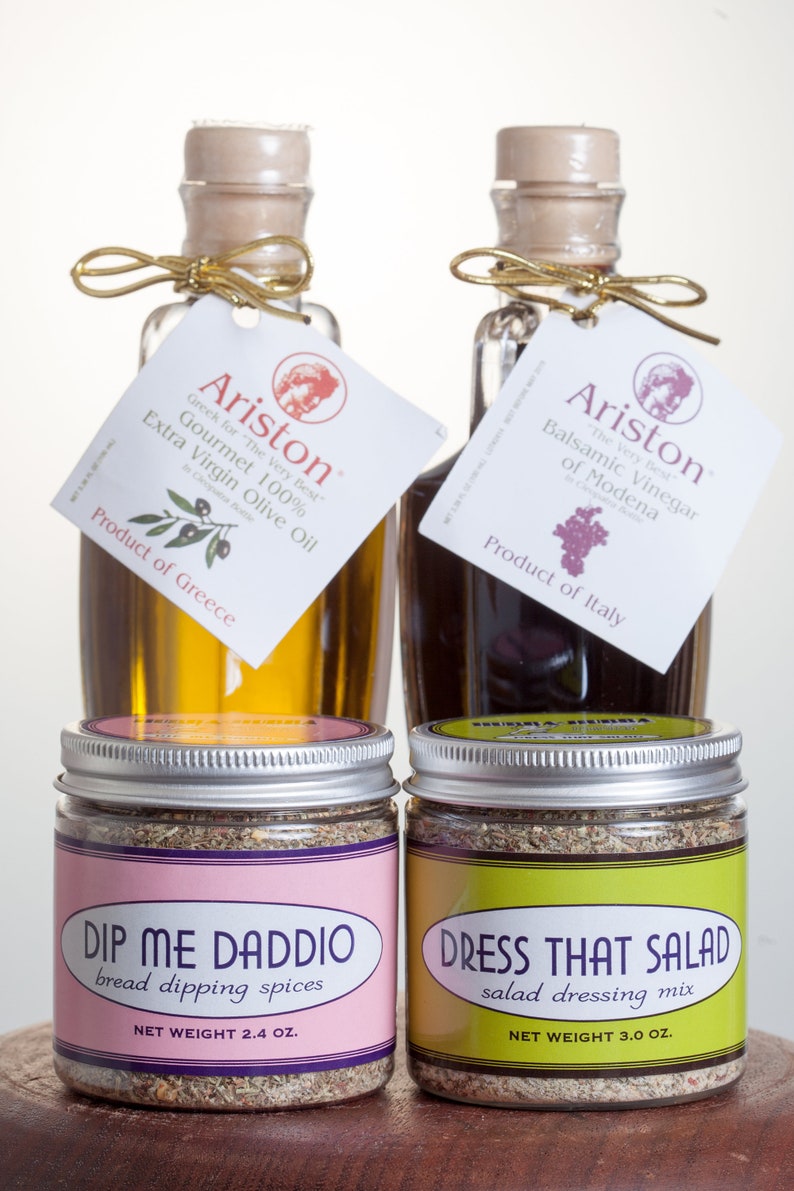 May include: Two glass bottles of olive oil and balsamic vinegar with labels that read "Ariston" and "Gourmet 100% Extra Virgin Olive Oil" and "Balsamic Vinegar of Modena". Two glass jars of spices with labels that read "Dip Me Daddi Bread Dipping Spices" and "Dress That Salad Salad Dressing Mix".